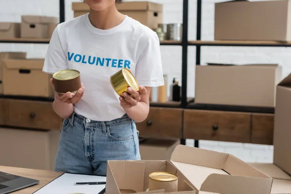 Cropped view of african american woman holding canned foodstuff while working in donation warehouse — Stock Photo