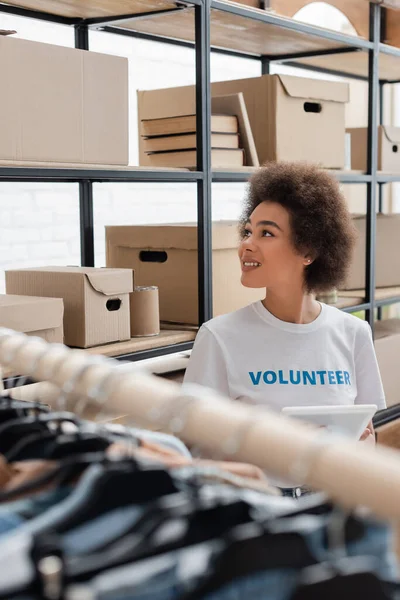 Sorrindo voluntário afro-americano olhando para rack com caixas de doação — Fotografia de Stock