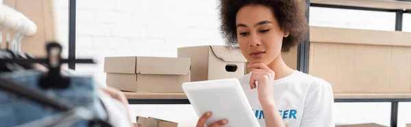 Pensive african american volunteer looking at digital tablet in charity center, banner — Stock Photo