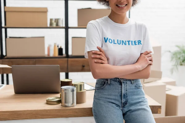 Cropped view of african american volunteer standing with crossed arms in charity storehouse — Fotografia de Stock