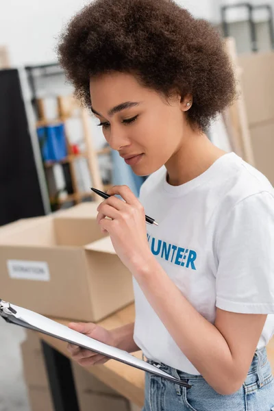 Mujer afroamericana bonita mirando portapapeles mientras trabaja en el centro de voluntarios - foto de stock