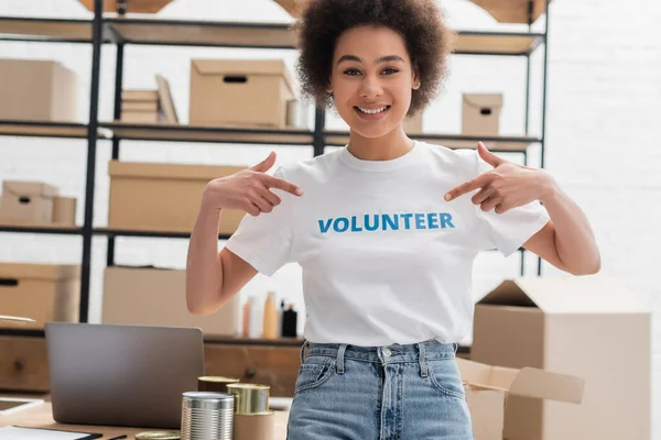 Erfreut afrikanisch-amerikanische Frau zeigt auf freiwillige Aufschrift auf T-Shirt — Stockfoto