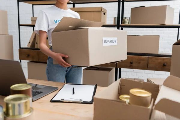 Cropped view of african american woman holding donation box in charity warehouse — Fotografia de Stock