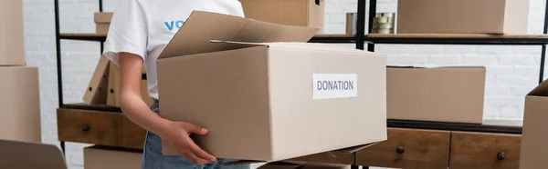 Vista recortada del voluntario afroamericano sosteniendo caja de donación en el centro de caridad, pancarta - foto de stock