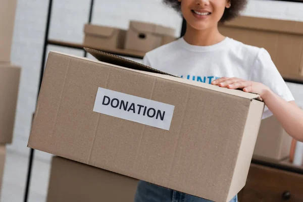 Vista recortada de borrosa mujer afroamericana caja de espera con letras de donación - foto de stock