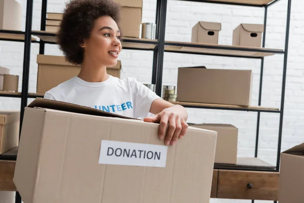 Jeune bénévole afro-américain tenant boîte de don dans un centre de charité — Photo de stock