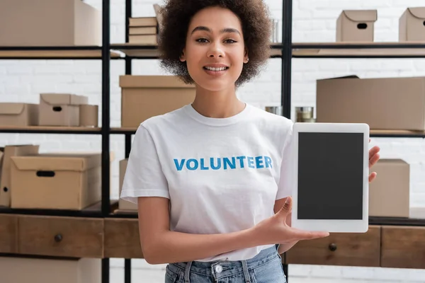 Heureux afro-américain bénévole souriant à la caméra près de tablette numérique avec écran blanc — Photo de stock