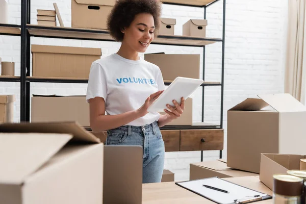 Sourire bénévole afro-américain en utilisant une tablette numérique tout en travaillant dans un entrepôt — Photo de stock