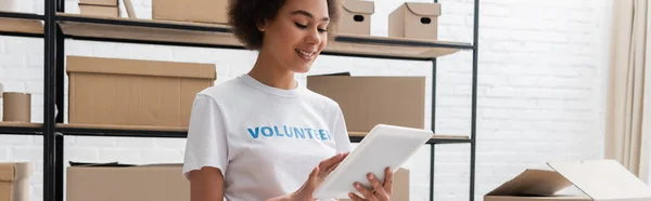 Voluntario afroamericano feliz usando tableta digital mientras trabaja en el centro de donación, pancarta - foto de stock