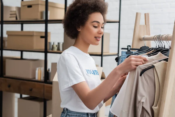 Sorridente afro-americano volontario ordinare vestiti nel centro di beneficenza — Foto stock