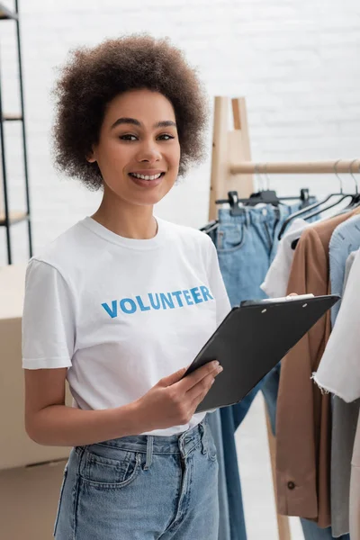Young african american woman with clipboard smiling at camera in volunteer center - foto de stock