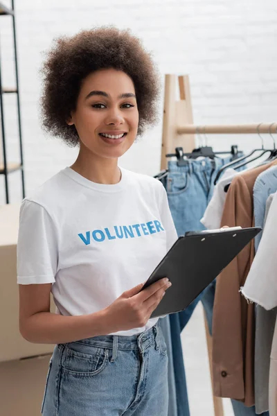 Young african american woman with clipboard smiling at camera in volunteer center — Photo de stock