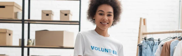 Bella donna afroamericana sorridente alla macchina fotografica nel centro di volontariato, striscione — Foto stock