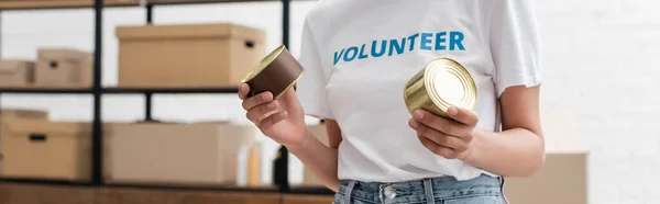 Partial view of african american volunteer holding canned food in charity warehouse, banner — Photo de stock