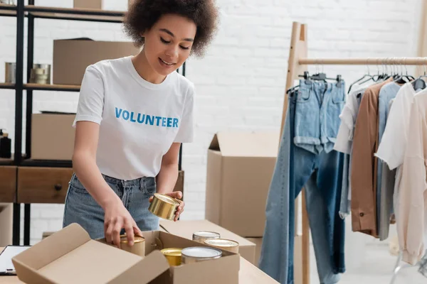 African american volunteer packing canned foodstuff in charity center — Stock Photo