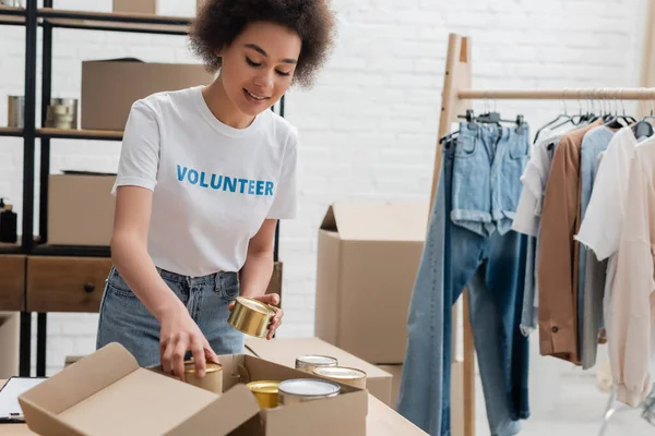 African american volunteer packing canned foodstuff in charity center — Photo de stock