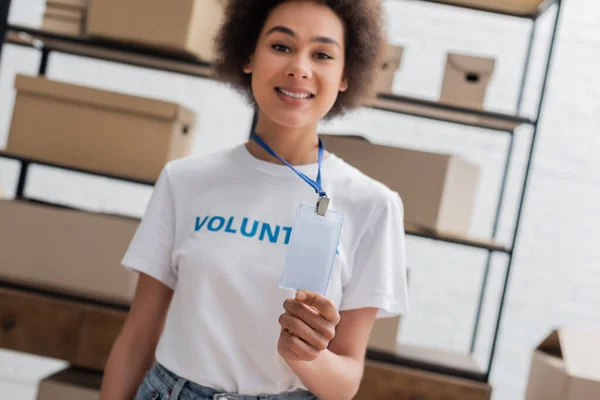 Blurred african american volunteer showing empty id card in charity storehouse — Stockfoto