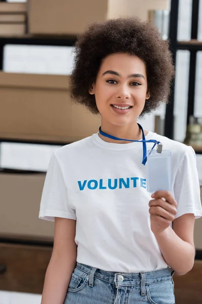 Sonriente mujer afroamericana sosteniendo etiqueta de nombre en blanco en el centro de voluntarios - foto de stock
