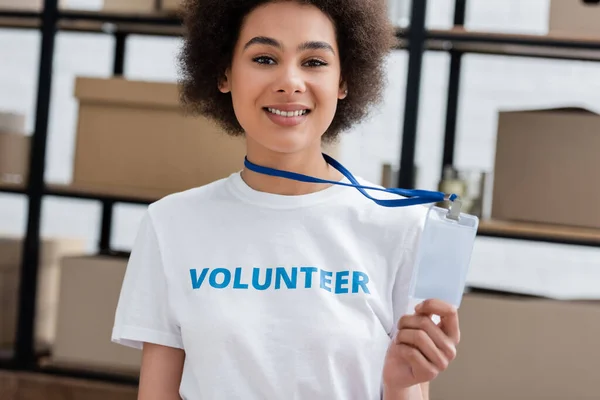 Cheerful african american volunteer showing blank id card in donation center - foto de stock