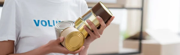 Vista recortada del voluntario afroamericano sosteniendo alimentos enlatados, pancarta - foto de stock