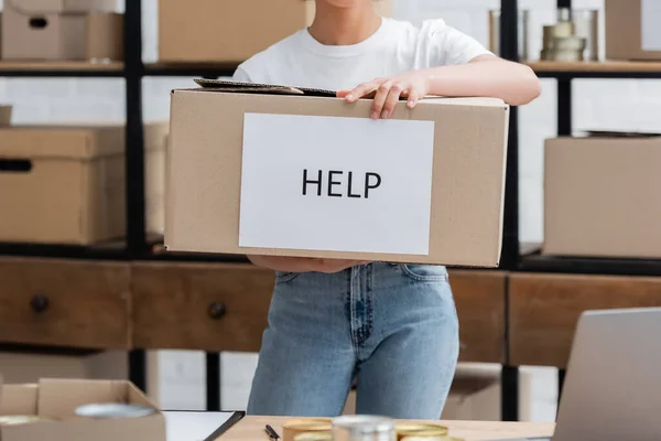 Partial view of african american volunteer holding box with help lettering in charity center - foto de stock