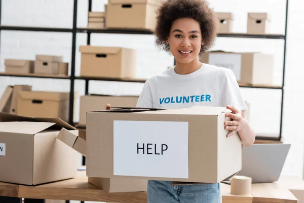 Heureux afro-américain bénévole tenant boîte de carton avec lettrage d'aide dans le centre de charité — Photo de stock