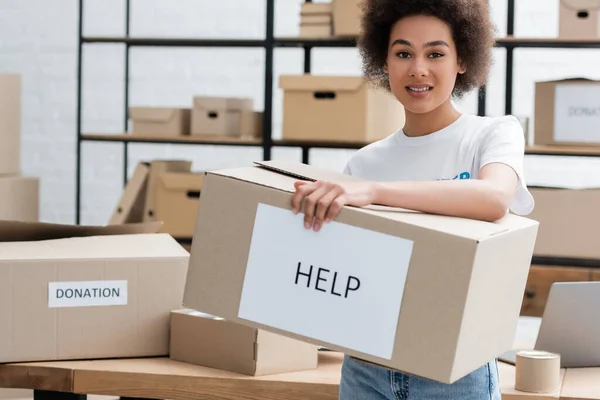 Donna afro-americana positiva che tiene la scatola con lettere di aiuto nel centro di volontariato — Foto stock