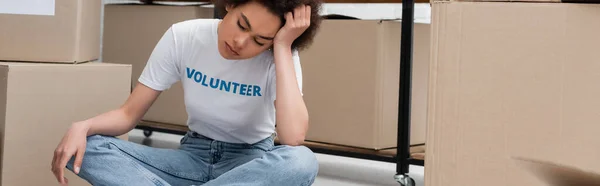 Exhausted african american volunteer sitting with crossed legs and closed eyes in charity center, banner - foto de stock