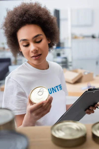 Afro-américaine femme tenant presse-papiers et de la nourriture en conserve dans le centre de charité — Photo de stock