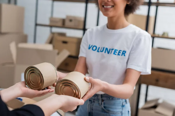 Vue recadrée d'un bénévole afro-américain souriant distribuant de la nourriture en conserve dans un centre caritatif — Photo de stock