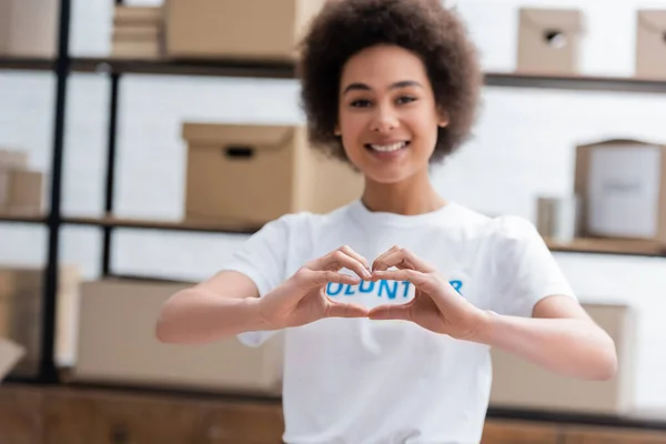 Alegre africano americano voluntario mostrando amor signo en borrosa fondo - foto de stock