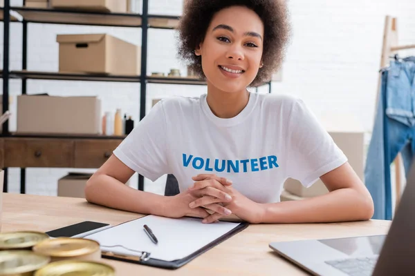 Voluntário afro-americano feliz olhando para a câmera no local de trabalho no centro de doação — Fotografia de Stock