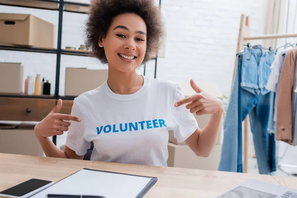 Femme afro-américaine souriante pointant du doigt le t-shirt avec un lettrage volontaire — Photo de stock