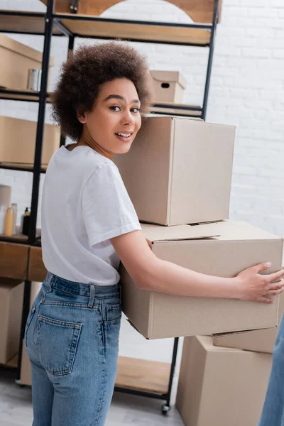 Smiling african american woman holding donation boxes in charity center — Fotografia de Stock