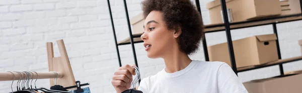 Young african american woman holding hangers while working in charity center, banner — Stock Photo
