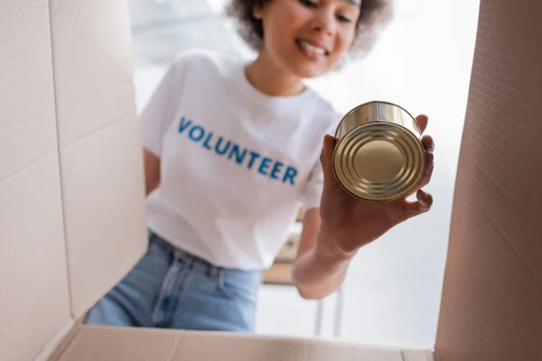 Vista inferior de Africano americano voluntário segurando lata perto caixa de papelão — Fotografia de Stock