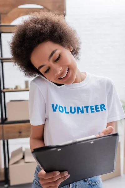 Glücklich afrikanisch-amerikanischer Freiwilliger spricht auf Smartphone neben verschwommenem Laptop in Charity-Zentrum — Stockfoto