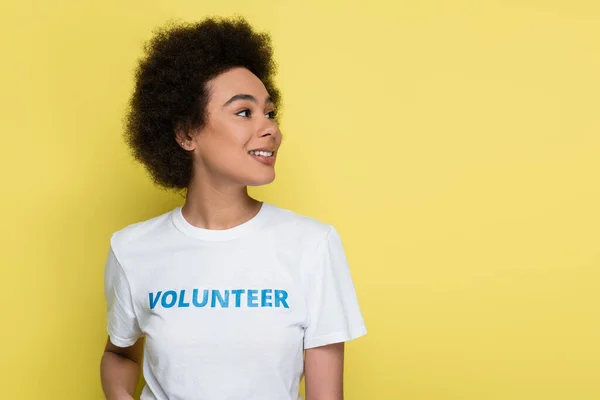 Heureuse femme afro-américaine avec lettrage bénévole sur t-shirt regardant loin isolé sur jaune — Photo de stock