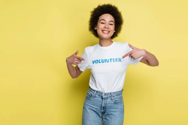 Excited african american woman pointing at volunteer lettering on t-shirt isolated on yellow — Foto stock