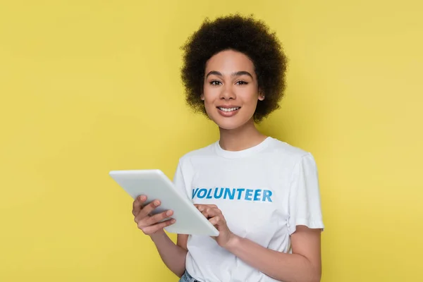 Voluntario afroamericano con tableta digital sonriendo a la cámara aislada en amarillo - foto de stock