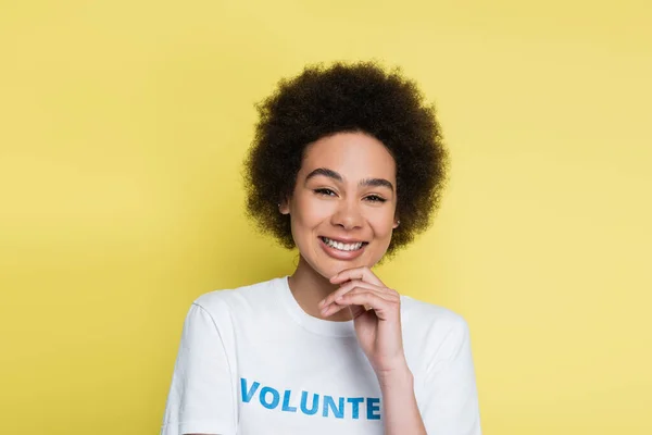 Happy african american volunteer touching chin and smiling at camera isolated on yellow — Stock Photo