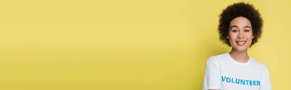 Curly african american woman in t-shirt with volunteer inscription isolated on yellow, banner — Stock Photo