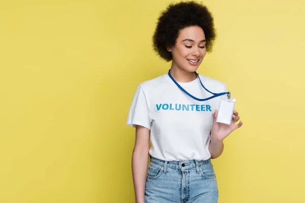 Smiling african american volunteer showing blank name tag isolated on yellow — Stockfoto