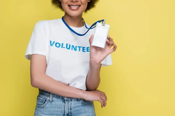 Vista recortada de sonriente afroamericano voluntario sosteniendo etiqueta de nombre en blanco aislado en amarillo - foto de stock