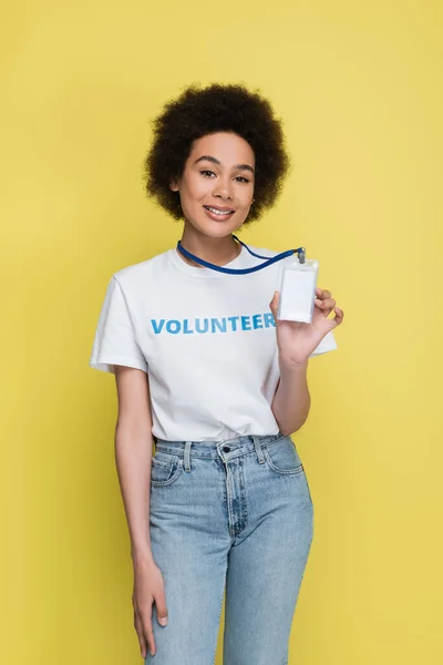 Smiling african american volunteer showing empty name tag isolated on yellow — Stockfoto