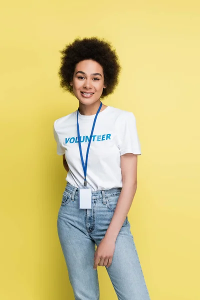 Young african american volunteer with blank name tag standing with hand behind back isolated on yellow — Stock Photo