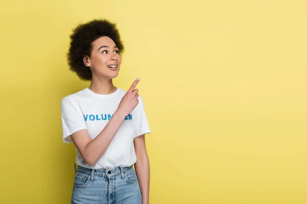 Happy african american volunteer looking away and pointing with finger isolated on yellow — Fotografia de Stock