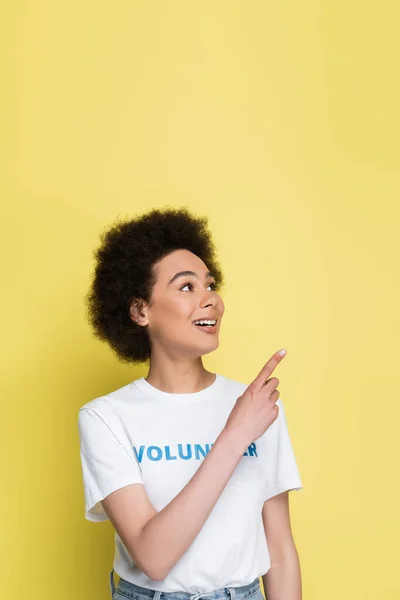 Positive african american volunteer looking away while pointing with finger isolated on yellow — Stockfoto