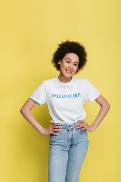 Pleased african american volunteer posing with hands on hips isolated on yellow — Stock Photo