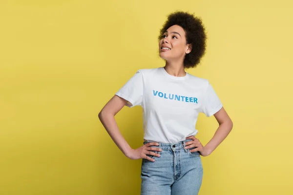 Pretty african american volunteer standing with hands on hips and looking away isolated on yellow — Foto stock